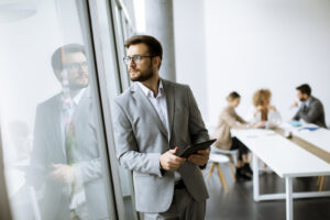 Young modern businessman using digital tablet in the office Male looking out windows
