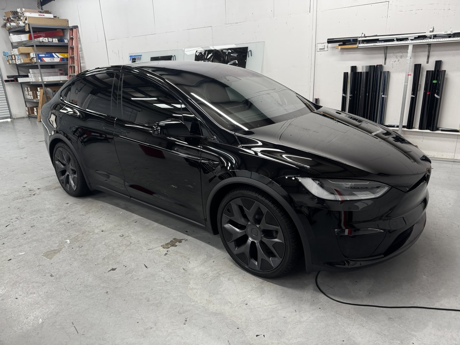Black Tesla Model X inside The Tint Guy shop with film rolls behind it